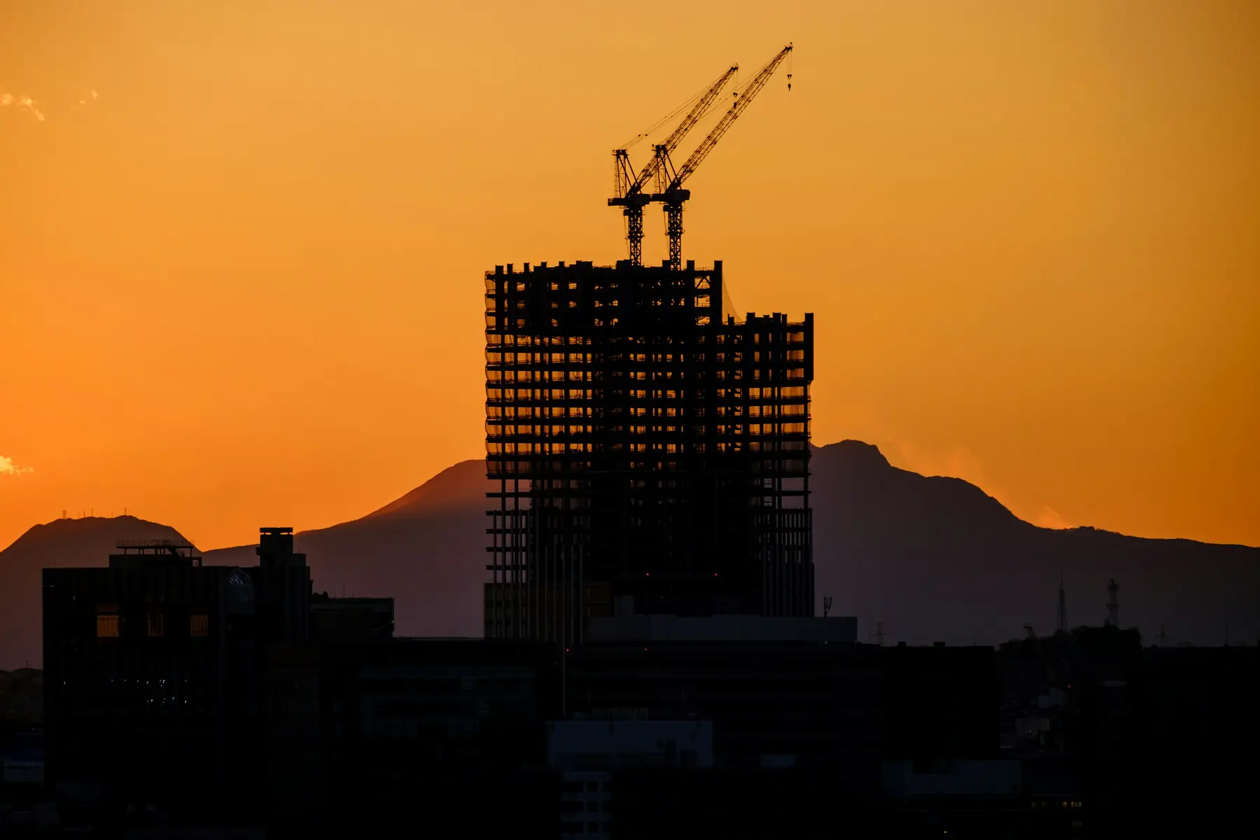 A tower under construction at dusk, cranes above it