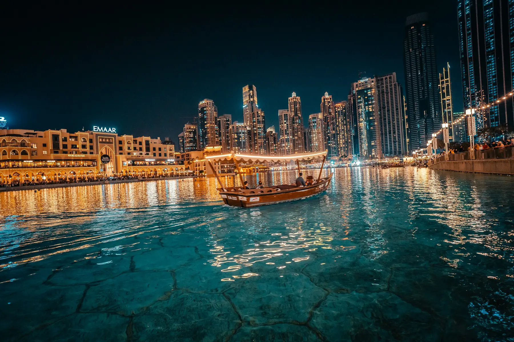 Dubai waterfront towers at night with a dhow on the water